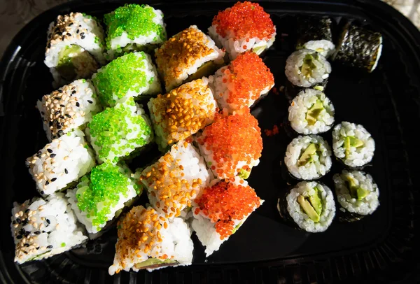 Close-up of sushi rolls with red caviar, salmon, tuna, and avocado isolated on black background.