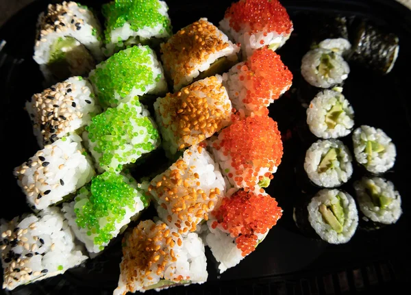 Close-up of sushi rolls with red caviar, salmon, tuna, and avocado isolated on black background.