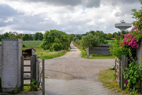 Rural landscape. Open gate to the farm and the road leading into the distance. Sky with rain clouds. High quality photo