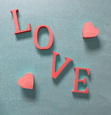 Yukarıdan gelen mavi arkaplandaki kırmızılı aşk sözcüğünün her iki tarafında iki pembe kalp.