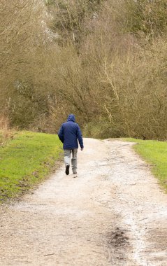 Yalnız bir adam, kapüşonlu bir bluz giyiyor. Kışlık kırsal kesimin portre oryantasyonunda toprak yolda yürüyor. 