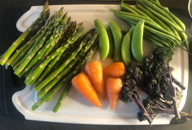 Pişirilmeyi bekleyen beyaz bir doğrama tahtasının üzerinde düzleşmiş sebzeler.