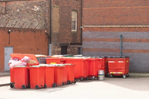 Side view on a row of red  recycling bins along a brick wall in a city alley, with space for text on top