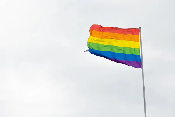 Gökkuşağı bayrağı, LGBT topluluğunun sembolü, bulutlu beyaz arka planda rüzgarda sallanan