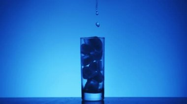 Mavi arka planda buzlu bir bardağa sıvı dökmek. Siluet.