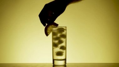 Adam limon, kiraz ve kokteyl bardağına saman koyuyor. Siluet. Sarı Arkaplan. Yavaş Hareket.