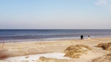 İnsanlar güneşli bir kış gününde deniz kıyısında yürürler.