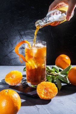 Chinotto drink in a glass with ice and citrus fruits on the grey table with pouring liquid from bottle clipart
