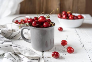 Beyaz ahşap arka planda peçeteli, ağlayıp sızlanan, gri kırsal fincanda tatlı kirazlar