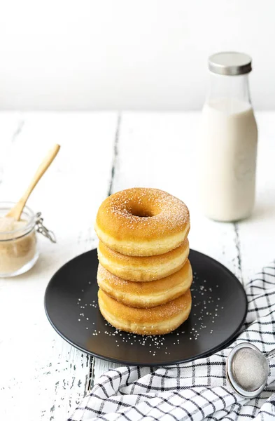 Doughnuts on black plate with sugar jar, milk bottle, small sieve and napkin — Stock Photo, Image
