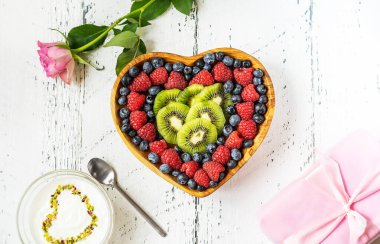 Sevgililer Günü kahvaltısı konsepti. Kalp şeklinde bir kase, yoğurt, gül ve hediyeye böğürtlen ve kivi karışımı.