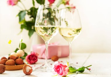 Sevgililer Günü konsepti. İki kadehte köpüklü şarap, litchi üzümü, güller ve hediye.