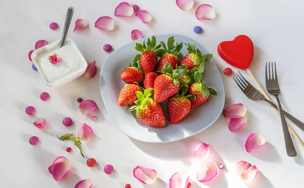 Concepto del Día de San Valentín. Fresas en plato gris claro, yogur, pétalos de rosa, corazón rojo de madera, dos tenedores —  Fotos de Stock