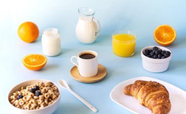 Bir fincan kahve, kruvasan, tam tahıllı halkalar, süt, portakal suyu, yoğurt ve yabanmersinli kahvaltı konsepti