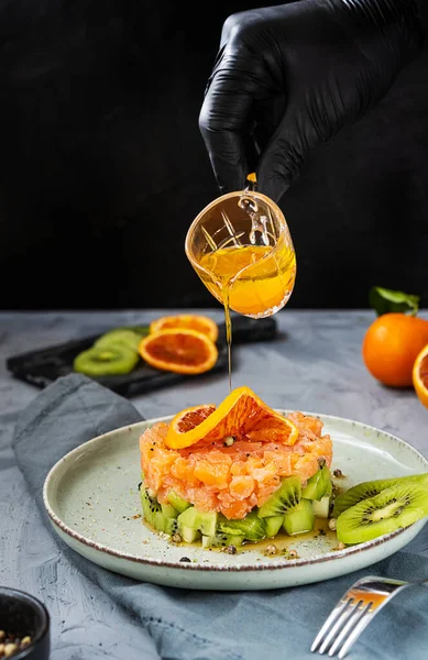 Delicioso salmão tartare com kiwi e molho de laranja no prato com mão chef — Fotografia de Stock