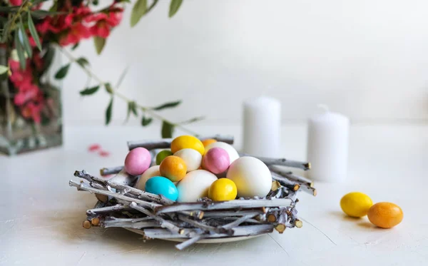 Paskalya için tatil kompozisyonu. Renkli ve beyaz yumurtalı yuva, mumlar, zeytin dalı ve bahar çiçekleri — Stok fotoğraf