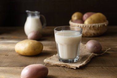 Bardakta vejetaryen patates sütü ve kırsal alanda çiğ patatesli süt kavanozu.