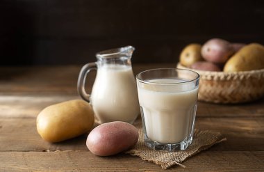 Bardakta vejetaryen patates sütü ve kırsal alanda çiğ patatesli süt kavanozu.
