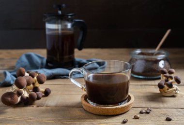 Kupada mantarlı kahve, kahve demliği, süt, kahve çekirdeği ve ahşap arka planda öğütülmüş kahve.