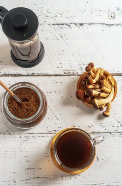 Sağlıklı, modaya uygun kahve, fincanda mantar, kahve demliği, beyaz ahşap arka planda çiğ mantar.