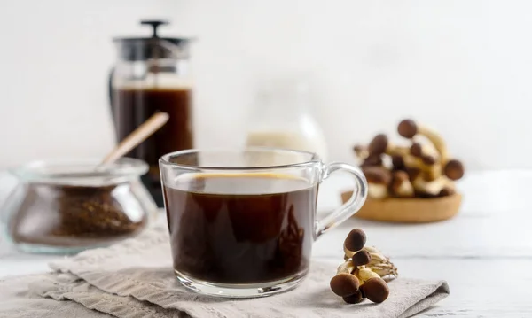 Sağlıklı moda kahve, fincanda mantar, kahve demliği, beyaz ahşap arka planda süt.