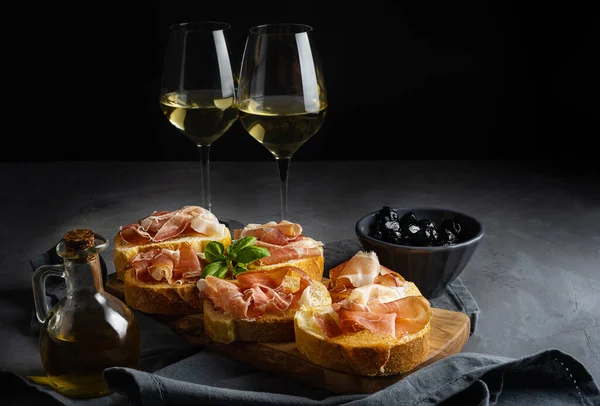 Aperitiv italian bruschetta cu prosciutto, vin alb. ulei de măsline și măsline negre — Fotografie, imagine de stoc