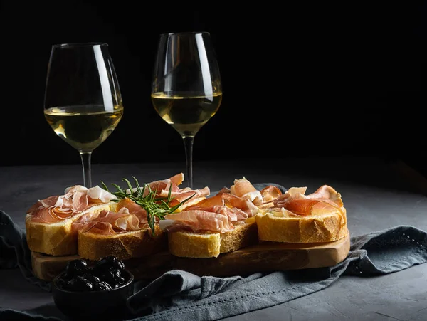Aperitiv italian bruschetta cu prosciutto, vin alb, ramură de rozmarin și măsline negre — Fotografie, imagine de stoc