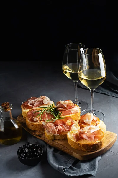 Aperitiv italian bruschetta cu prosciutto, vin alb, ramură de rozmarin, ulei de măsline și măsline negre — Fotografie, imagine de stoc