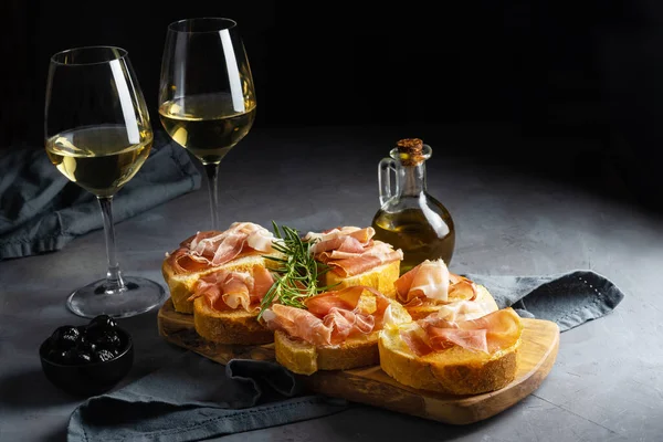 İtalyan aperatifi - jambonlu bruschetta, beyaz şarap, biberiye dalı ve siyah zeytin.