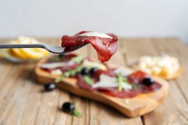 Limon, grana, zeytin ve roka ile çatalın üzerinde kurutulmuş et.