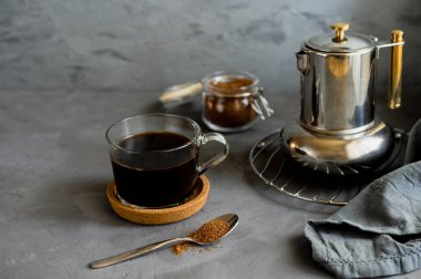 Fincanda taze demlenmiş kahve ve gri arka planda kamış şekerli kahve demliği.