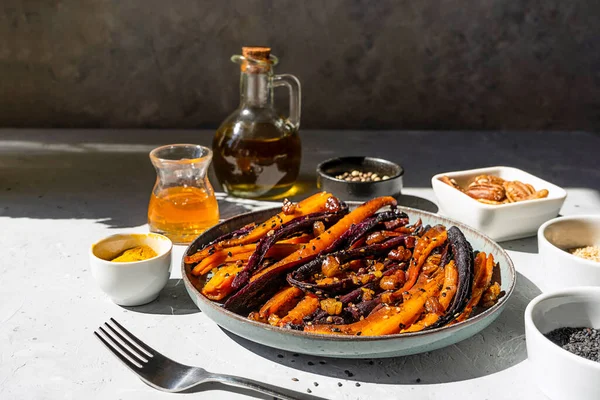 Roasted glazed spicy violet and orange carrots with ingredients on grey background. Close up — Fotografie, imagine de stoc