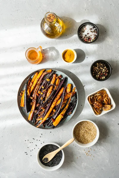 Baked glazed spicy violet and orange carrots with ingredients on grey background. Top view — Fotografie, imagine de stoc