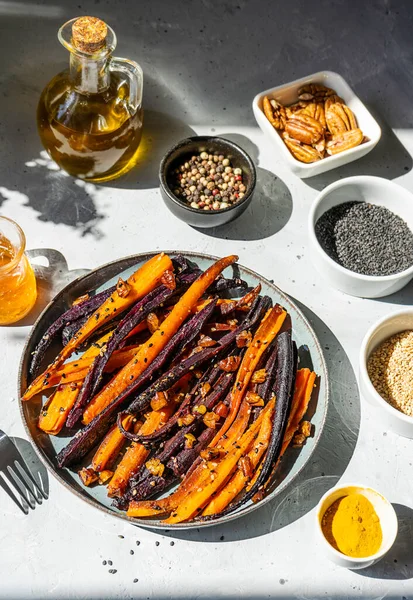 Baked glazed spicy violet and orange carrots with ingredients on grey background. Top view — Fotografie, imagine de stoc