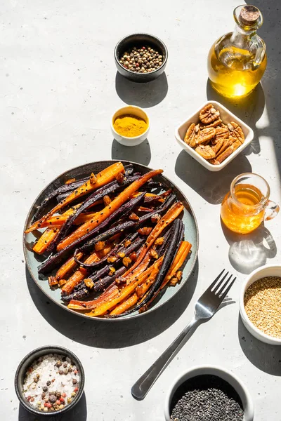 Baked glazed spicy violet and orange carrots with ingredients on grey background. Top view — Fotografie, imagine de stoc