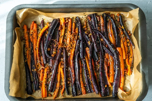 Roasted glazed spicy violet and orange carrots on baked sheet. Top view — Fotografie, imagine de stoc