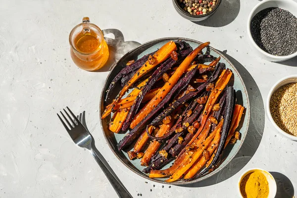Roasted glazed spicy violet and orange carrots with ingredients on grey background. Top view — Fotografie, imagine de stoc