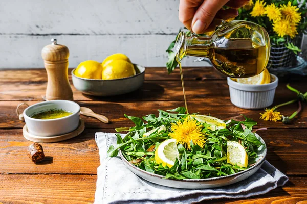 Dandelion salad with olive oil, lemon juice and spices on brown wooden table. Human hand pouring olive oil to dish. — Fotografie, imagine de stoc