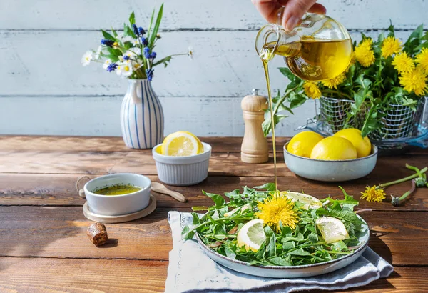 Salada de dente de leão com azeite, suco de limão e especiarias na mesa de madeira marrom. Mão humana derramando azeite para prato. — Fotografia de Stock