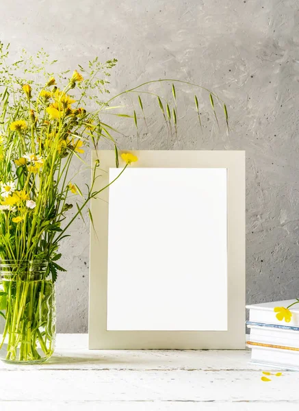 Mock up creation. White frame on white wooden table with grey concrete background and wild spring flowers