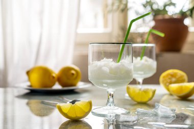 Limonlu limonlu limon şerbeti, buz küpleri ve gri arka plan ve pencerenin arkasında pipet içmek.