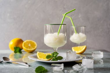 Limonlu, buzlu, nane yapraklı ve gri arka planda pipetli iki bardak limon şerbeti.