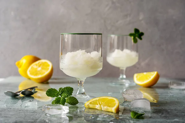 Lemon sorbet in two glasses with lemons, ice cubes, mint leaves on grey background — Stock Photo, Image