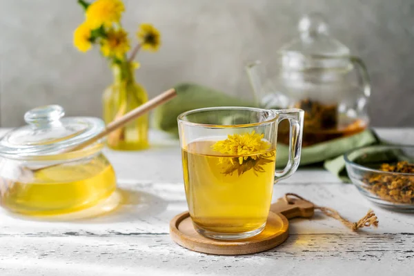 Dandelion tea and honey on the white wooden table with tea pot, dandelion flowers, dry mix for tea