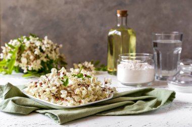 Tabakta Acacia çiçekleri ve beton zeminde Acacia böreği pişirmek için malzemeler var. 