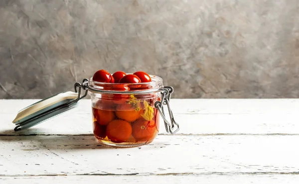 Pickled tomatoes in a glass jar on white wooden table with grey background and copy space — Stock Photo, Image
