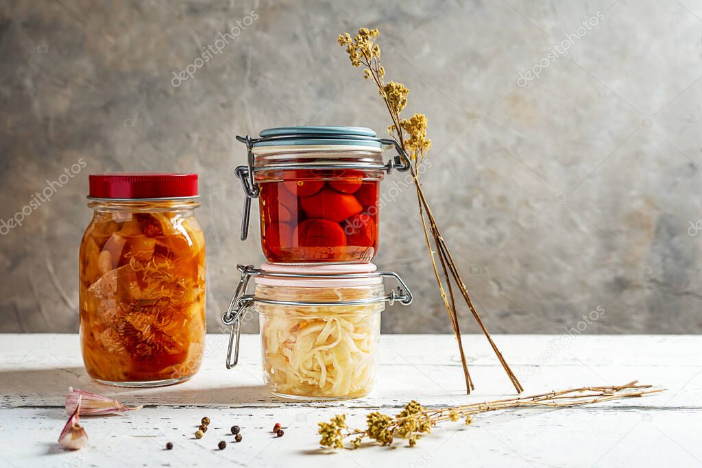 Pickled tomatoes, kimchi, cabbage in jar with garlic, pepper and oregano on white wooden table with grey background