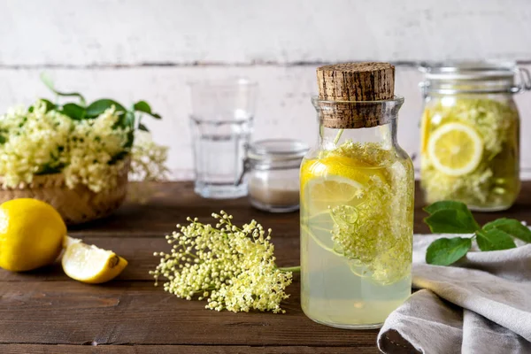 Elderberry infused watering or syrup made with water, fresh flowers, sugar and lemons as main ingredients. White and brown wooden background. Selective focus