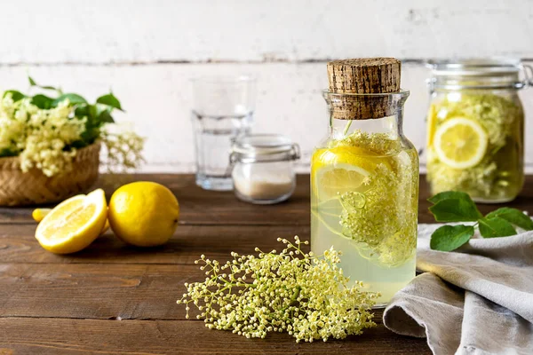 Elderberry infused watering or syrup made with water, fresh flowers, sugar and lemons as main ingredients. White and brown wooden background. Selective focus