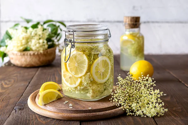 Elderberry infused watering or syrup in jar and bottle made with water, fresh flowers and lemons as main ingredients.Wooden background. Selective focus